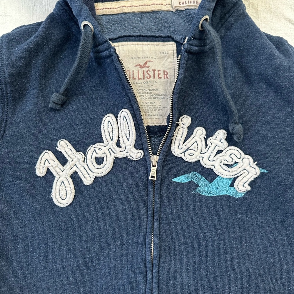 Hollister Navy Blue Zip-Up Hoodie with White Script and Teal Logo